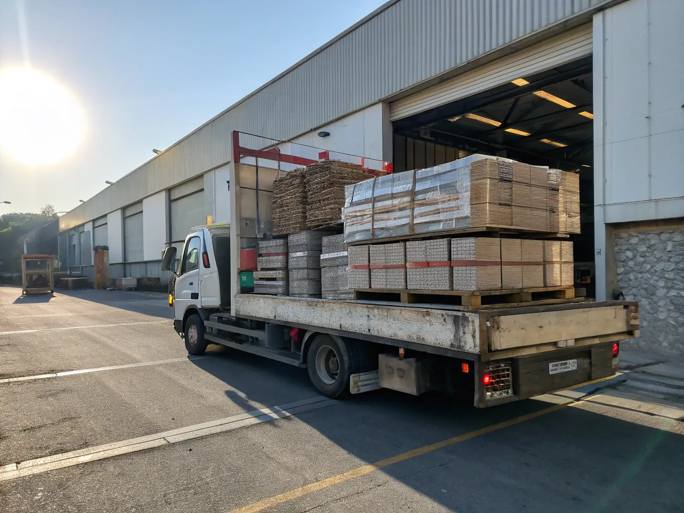 A delivery truck arriving at a warehouse, with workers unloading goods and a supervisor overseeing the process, representing final-mile delivery and distribution.